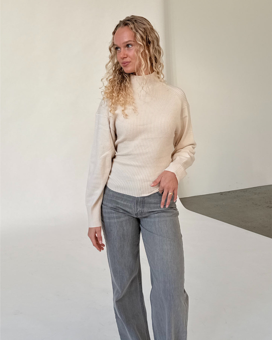 Modelfoto af pige i beige WHITNEY strik, samt grå NANNA jeans. Alt er fra BySofieSønderby.