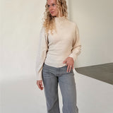 Modelfoto af pige i beige WHITNEY strik, samt grå NANNA jeans. Alt er fra BySofieSønderby.