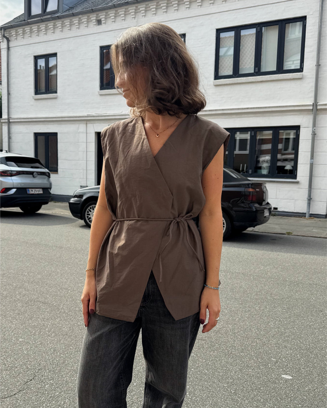 Modelfoto af pige i brun Yui vest med bindebånd, samt grå Nanna jeans. Alt er fra BySofieSønderby