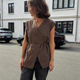 Modelfoto af pige i brun Yui vest med bindebånd, samt grå Nanna jeans. Alt er fra BySofieSønderby