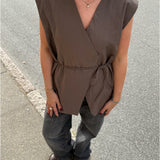 Modelfoto af pige i brun Yui vest med bindebånd, samt grå Nanna jeans. Alt er fra BySofieSønderby
